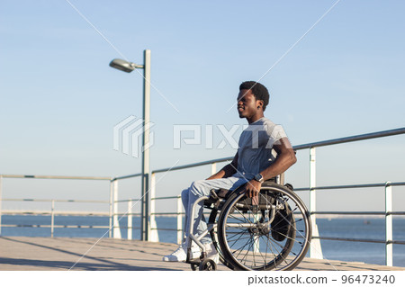 Young Black man in wheelchair enjoying spending time at seashore Young Black man in wheelchair enjoying spending time at seashore 96473240