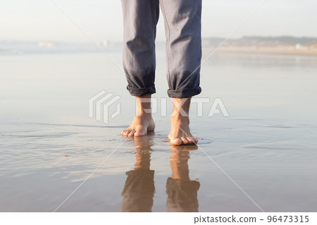 Close-up of male bare feet on wet sand Close-up of male bare feet on wet sand 96473315