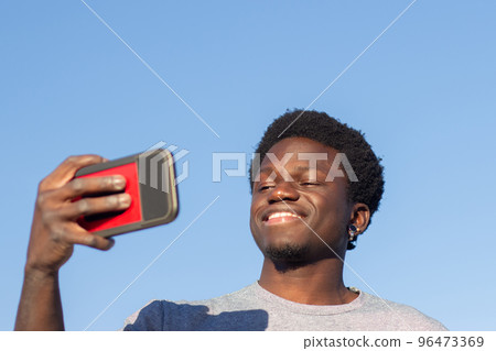 Happy Black guy taking selfie on his mobile phone outdoors 96473369
