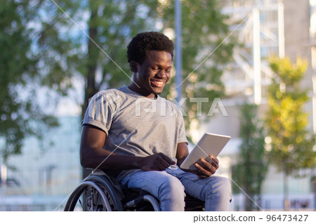 Young guy in wheelchair using his digital tablet in park 96473427