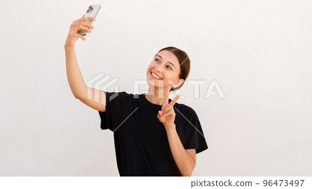 Portrait of happy woman making victory gesture and taking selfie Portrait of happy woman making victory gesture and taking selfie 96473497