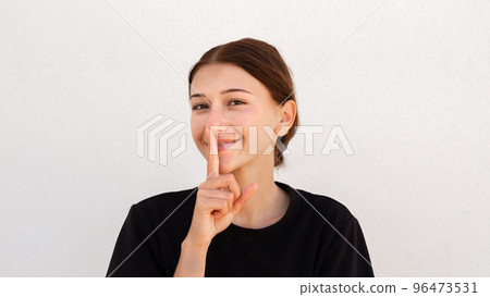 Portrait of flirty young woman posing with finger on lips 96473531