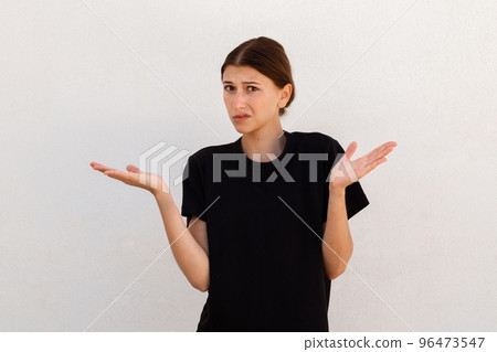 Portrait of displeased young woman shrugging shoulders 96473547