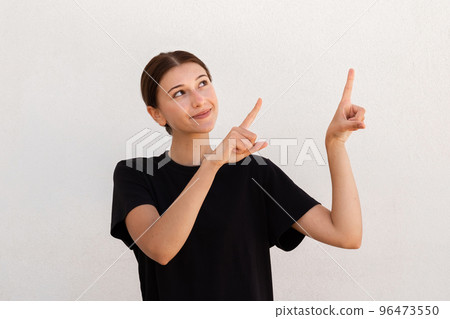 Portrait of positive young woman pointing forefingers upwards Portrait of positive young woman pointing forefingers upwards 96473550