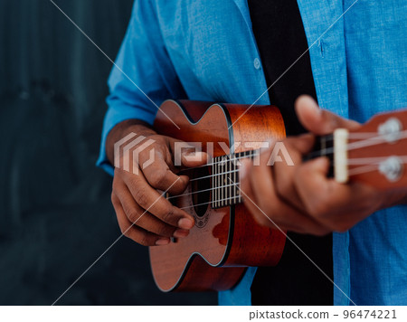 Indian young man in a blue shirt and glasses playing the guitar in front of the school blackboard Indian young man in a blue shirt and glasses playing the guitar in front of the school blackboard 96474221