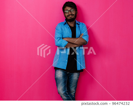 Indian smiling young student in blue shirt and glasses posing on pink background Indian smiling young student in blue shirt and glasses posing on pink background 96474232