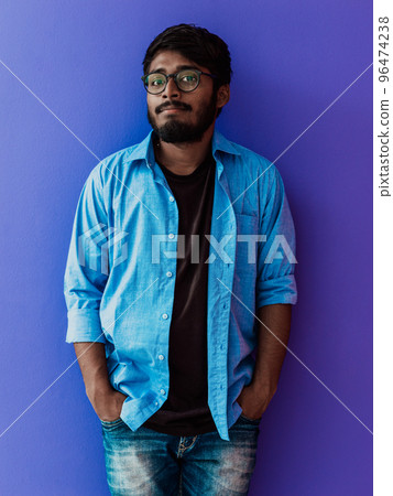 Indian smiling young man with blue shirt and glasses posing on purple background 96474238