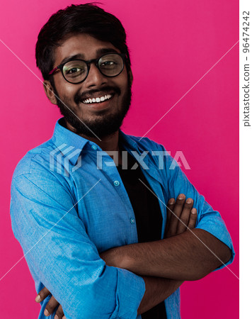 Indian smiling young man with blue shirt and glasses posing on pink background Indian smiling young man with blue shirt and glasses posing on pink background 96474242