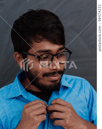 Indian young student wearing glasses puts on a blue shirt while standing in front of the school blackboard Indian young student wearing glasses puts on a blue shirt while standing in front of the school blackboard 96474251