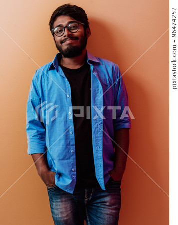Indian smiling young student in blue shirt and glasses posing on orange background 96474252