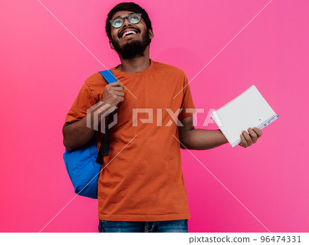 Indian student with blue backpack, glasses and notebook posing on pink background. The concept of education and schooling. Time to go back to school Indian student with blue backpack, glasses and notebook posing on pink background. The concept of education and schooling. Time to go back to school 96474331