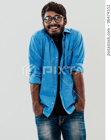 Indian smiling young man with blue shirt and glasses posing on gray background 96474352