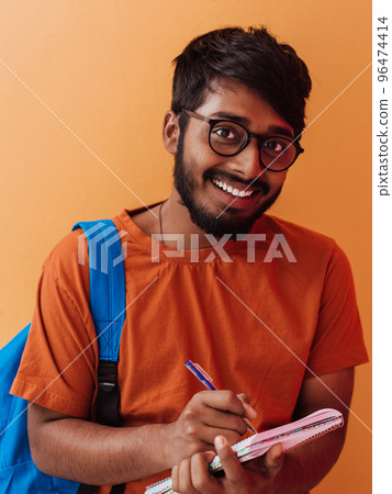 Indian student with blue backpack, glasses and notebook posing on orange background. The concept of education and schooling. Time to go back to school 96474414