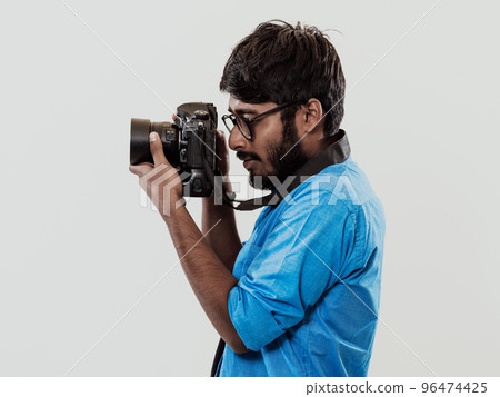 Professional photographer having DSLR camera taking picture.Indian man photography enthusiast taking photo while standing on blue background. Studio shot 96474425