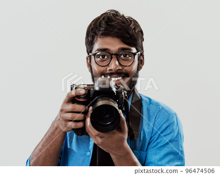 Professional photographer having DSLR camera taking picture.Indian man photography enthusiast taking photo while standing on blue background. Studio shot 96474506