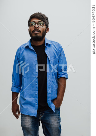 Indian smiling young man with blue shirt and glasses posing on gray background Indian smiling young man with blue shirt and glasses posing on gray background 96474535