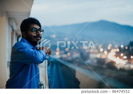 An Indian man with glasses and a blue shirt looks around the city at night. In the background of the night street of the city 96474552