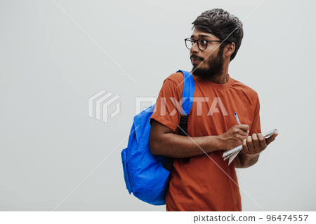 Indian student with blue backpack, glasses and notebook posing on gray background. The concept of education and schooling. Time to go back to school Indian student with blue backpack, glasses and notebook posing on gray background. The concept of education and schooling. Time to go back to school 96474557