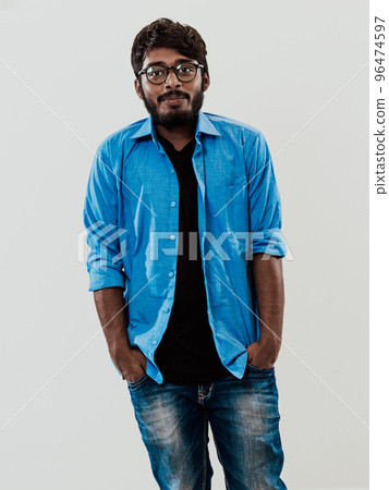 Indian smiling young man with blue shirt and glasses posing on gray background 96474597