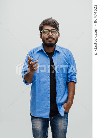 Indian smiling young man with blue shirt and glasses posing on gray background Indian smiling young man with blue shirt and glasses posing on gray background 96474622
