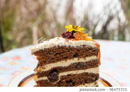 Close-up of a delicious carrot cake decorated with an edible flowers on a plate. Close-up of a delicious carrot cake decorated with an edible flowers on a plate. 96475723