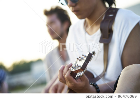 young asian adult men sitting on beach relaxing and playing guitar 96476069