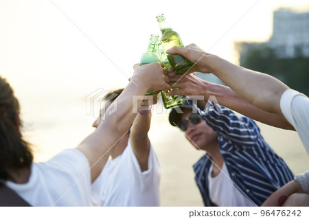 group of young asian adult men sitting on beach toasting with bottles of beer 96476242