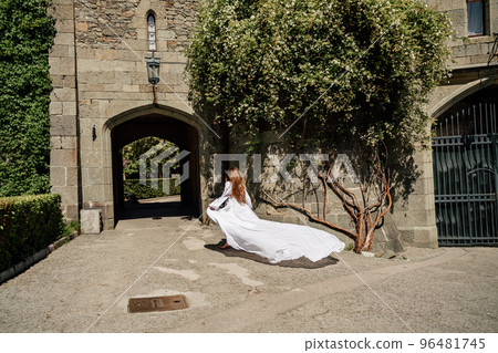 a beautiful woman in a white dress walks through a beautiful palace on a sunny day 96481745