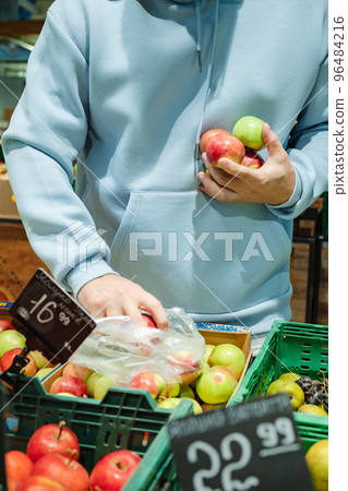 A man buys food, . A male customer chooses apples, taking products from the shelves 96484216