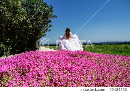 a beautiful woman in a white flowing long dress stay near a beautiful field with pink flowers rear view a beautiful woman in a white flowing long dress stay near a beautiful field with pink flowers rear view 96484280