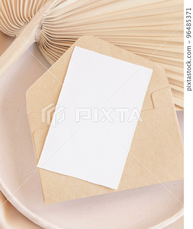 Card and envelope on plate on dried palm leaf and beige silky fabric close up, greeting or wedding mockup 96485371