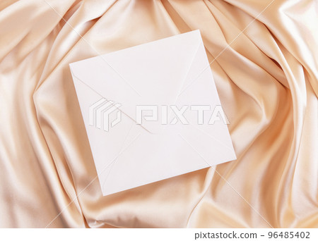 Square envelope on beige silky fabric drapery top view, greeting or wedding mockup 96485402