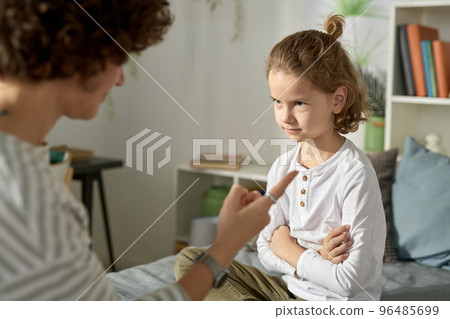 Naughty boy sitting on bed with his arms crossed and listening to his mom talking about his bad behavior Naughty boy sitting on bed with his arms crossed and listening to his mom talking about his bad behavior 96485699