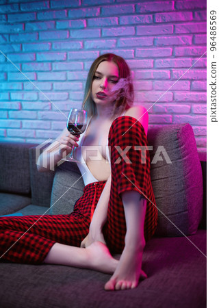 sexy liberated girl in sexy clothes smokes and drinks alcohol at a party in neon light 96486569