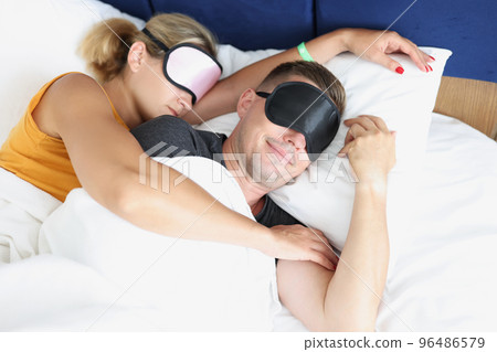Couple in sleeping masks in bed together embracing 96486579