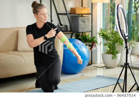 Fitness trainer filming herself applying elastic therapeutic tape on arm 96487014