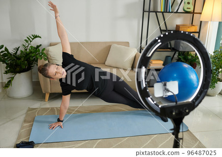 Online fitness instructor filming herself doing side plank Online fitness instructor filming herself doing side plank 96487025