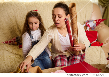 Loving mom and daughter enjoy the upcoming winter holidays, packing unwrapping Christmas New Year presents gift boxes at home together. Merry Christmas and Happy New Year! Holiday and family event 96487219