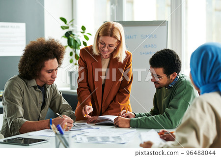 Successful teacher consulting one of students at lesson Successful teacher consulting one of students at lesson 96488044