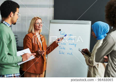 Confident mature teacher of English language pointing at whiteboard 96488065