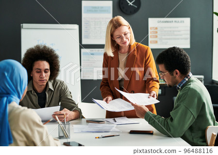 Happy mature blond teacher passing grammar tests to students Happy mature blond teacher passing grammar tests to students 96488116