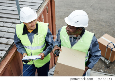 Two smiling workers carrying boxes at shipping docks Two smiling workers carrying boxes at shipping docks 96488234