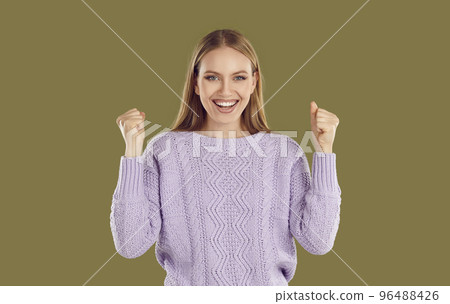 Overjoyed happy young blondy woman in purple sweater showing yes gesture on khaki background. 96488426