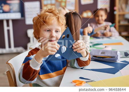 Cute primary school learner holding blue paper with holes for eyes and mouth 96488644