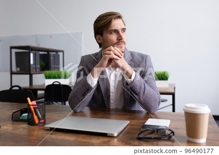stylish young businessman pensive sitting at the table in the office stylish young businessman pensive sitting at the table in the office 96490177
