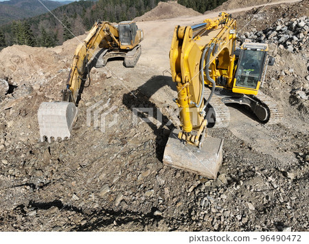 Industrial mine excavators are digging the soil in the construction site and loading trucks. Aerial drone top view. Industrial mine excavators are digging the soil in the construction site and loading trucks. Aerial drone top view. 96490472