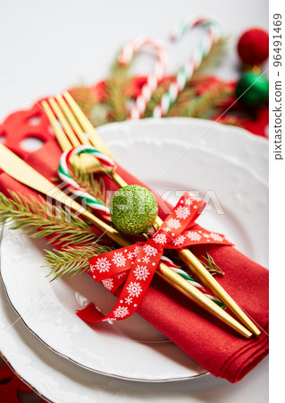 Christmas festive table setting with white plates and gold cutlery, red linen napkin, fir branches, red and green balls Christmas festive table setting with white plates and gold cutlery, red linen napkin, fir branches, red and green balls 96491469