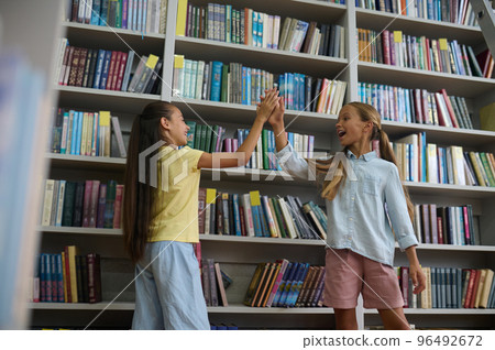 Girls standing near the high book shelves in the school library 96492672