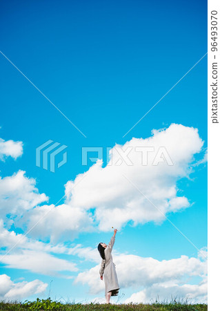 A woman with long hair reaching out under the vast blue sky 96493070