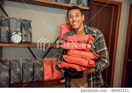 Joyful worker standing in a storeroom beside shelves with goods Joyful worker standing in a storeroom beside shelves with goods 96493523